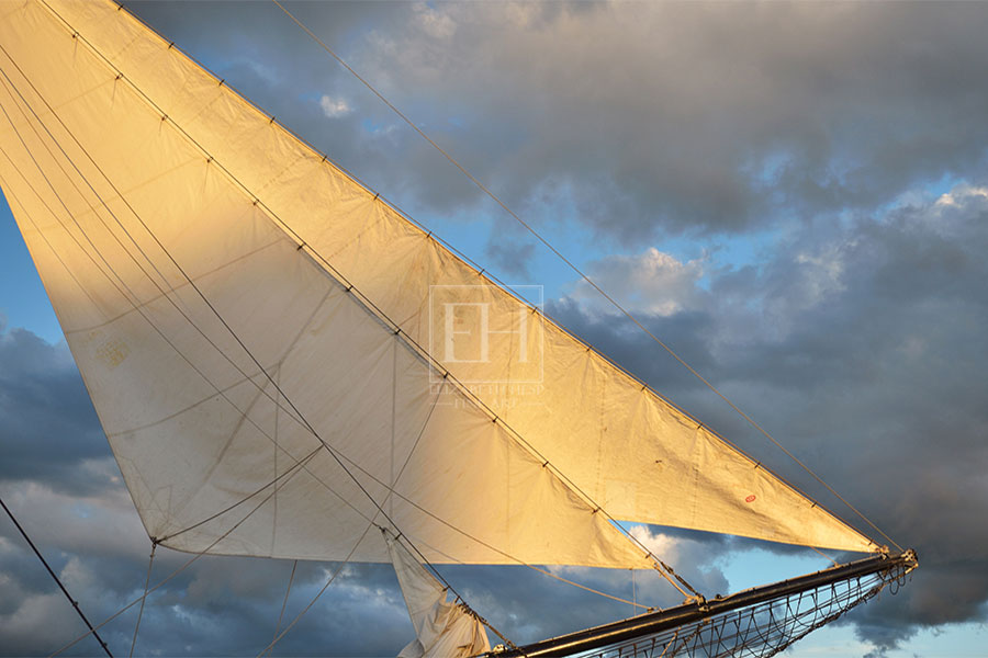 Sails of Tall ship glowing golden in the light of the setting sun.